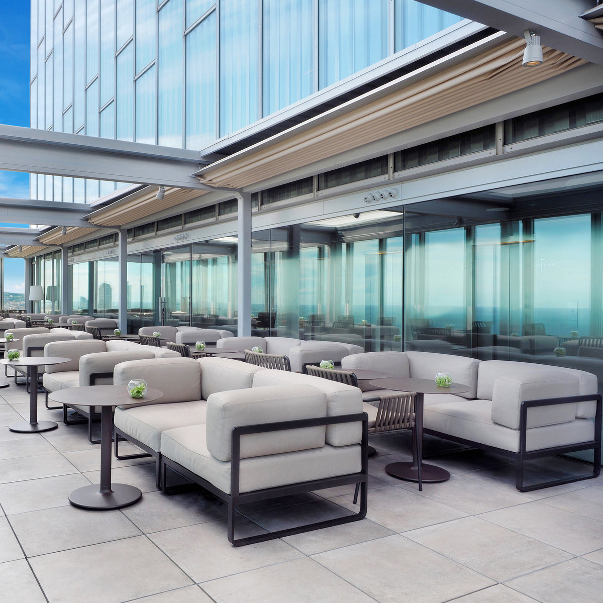 Sit modular garden sofa sections with light grey cushions and anthracite aluminium frames, arranged on a rooftop terrace with dark side tables.