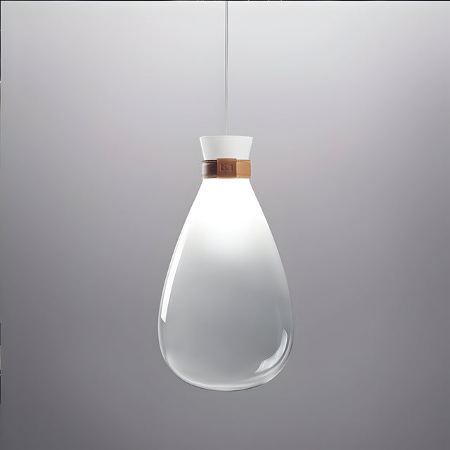 The Soffi Small Glass Pendant Light - Clear showcases a modern design with its sleek, teardrop-shaped shade and handcrafted elegance. Hanging from the ceiling, it emits a soft glow and features a metallic accent near the top against its simple gray backdrop, epitomizing minimalist lighting at its best.