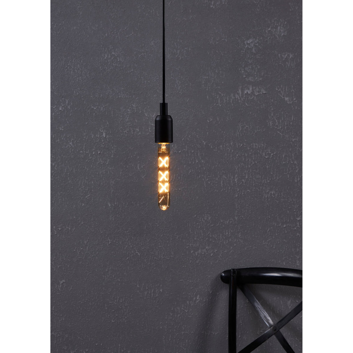 Pendant light fitted with a Smart Amber LED Bulb E27, its slim glass tube showing X-shaped filaments glowing warm white, hung against a dark textured wall.
