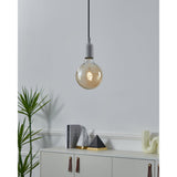 Smart LED globe bulb G125 with amber glass, spiral filament, and brass-coloured E27 screw base, shown lit on a grey pendant fitting in a living room setting.