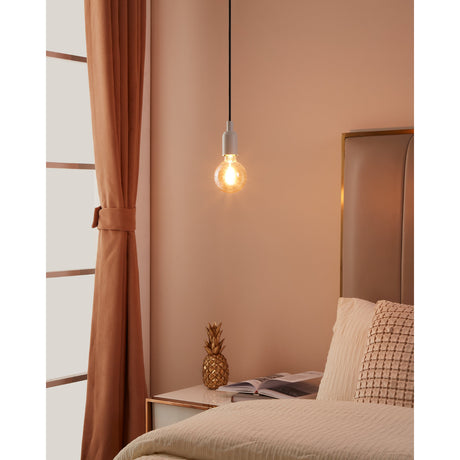 Smart Amber LED Globe Bulb E27 G95 7W lit on a pendant cord above a bedside table in a pink-toned bedroom, showing its spiral filament and rounded glass shape.