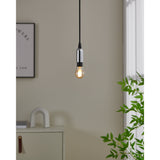 Smart Amber LED Golf Ball Bulb E14, lit pendant with black cord and chrome holder, hanging in a neutral living room near a framed print and plant.