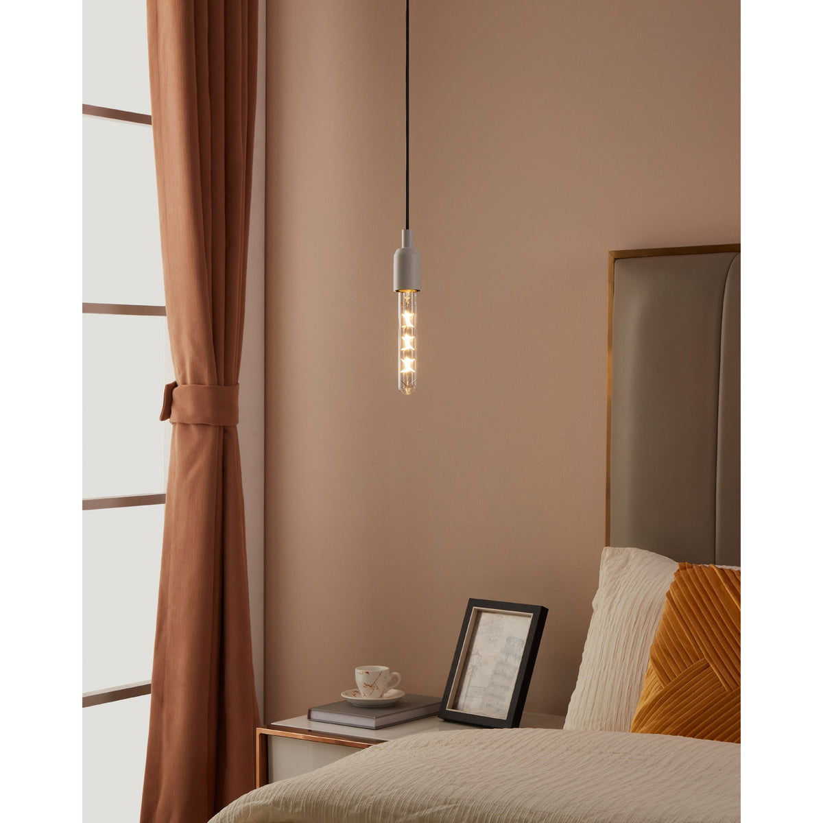 Pendant light with clear tubular LED bulb, E27 fitting, crossed filament design, warm white glow, shown above a bedside table in a bedroom setting.