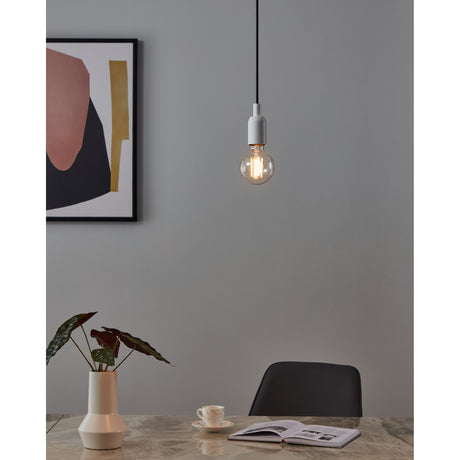 Smart Clear LED Globe Bulb E27 G80 lit in a pendant fixture with white ceiling cap and black cable, shown above a dining table in a grey-walled room.