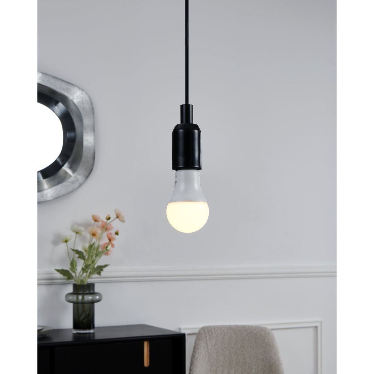 Smart LED GLS bulb with opal shade and black E27 fitting, pendant-mounted and lit warm white above a sideboard with mirror and flowers.