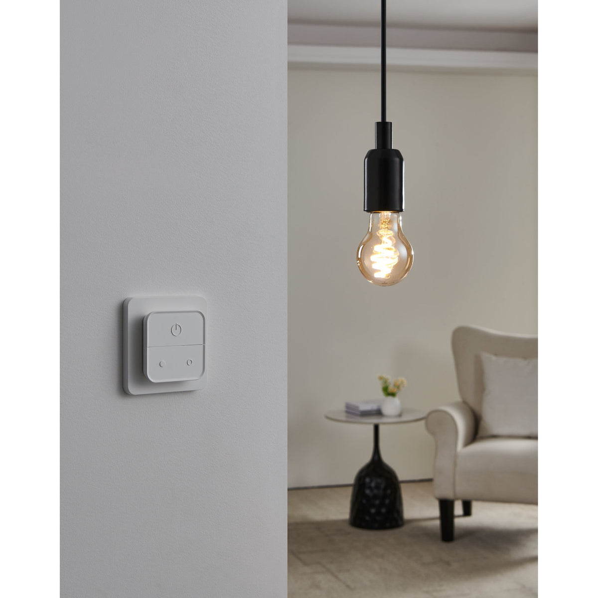 Smart LED GLS bulb E27 with amber glass and spiral filament, lit in a black pendant fitting above a wall-mounted smart dimmer switch in a living room.