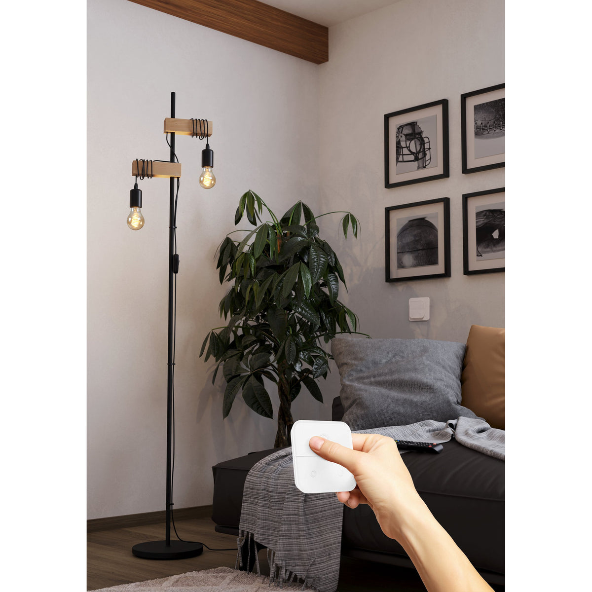 Smart LED GLS bulbs, E27 fitting, amber-tinted glass with spiral filament, lit on a black floor lamp beside a plant, controlled via handheld smart remote in a living room.