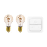 Two Smart LED GLS bulbs, E27, with amber-tinted glass and visible spiral filament, shown beside a white smart dimmer switch with push-button and dial controls on a plain white background.