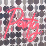 Party Neon Sign in pink script script-style LED tubing mounted on a clear square panel, set against a shimmering silver sequin backdrop.