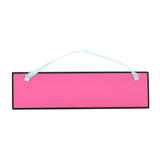 Rectangular wooden hanging plaque with a hot pink panel and black frame, blank of text, hung by a pale blue ribbon on a plain white background.