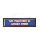 Black wooden hanging plaque with gold inner edge, reading "All You Need Is Love & Wine" in pink and yellow lettering on a blue background, on a light ribbon.