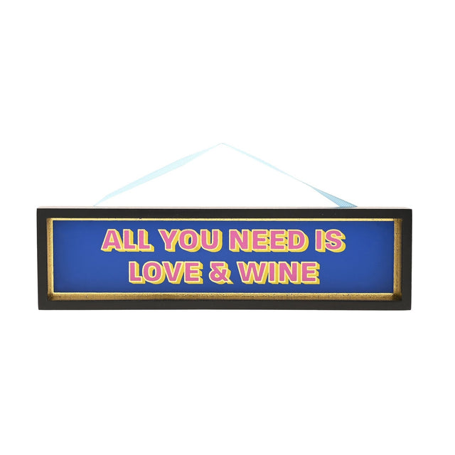 Black wooden hanging plaque with gold inner edge, reading "All You Need Is Love & Wine" in pink and yellow lettering on a blue background, on a light ribbon.