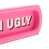 Close-up of the pink wooden "Better Late Than Ugly" wall plaque, showing bold shadowed lettering in a recessed panel with a gold-lined raised border.
