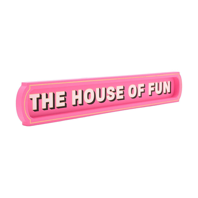 Pink wooden wall plaque reading "THE HOUSE OF FUN" in bold pale pink capitals with black shadow and gold outline, raised border with gold pin line, shown on a white background.