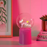 Be You Tiful Globe LED Neon Ceramic Table Lamp 22cm in pink, clear round globe with "BE you TIFUL" script and heart detail on a tall pink ceramic base, shown on a desk.