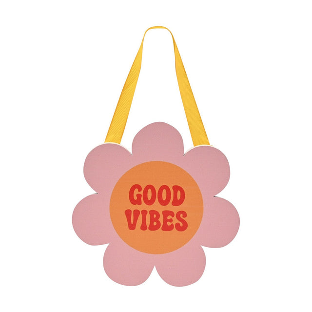 Wooden flower-shaped wall plaque in pink with an orange centre reading "Good Vibes" in red lettering, hung on a yellow ribbon against a plain white background.