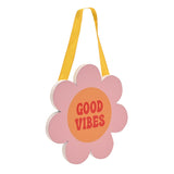 Pink wooden flower-shaped hanging plaque with orange centre reading "Good Vibes" in red lettering, suspended on a yellow ribbon against a plain white background.