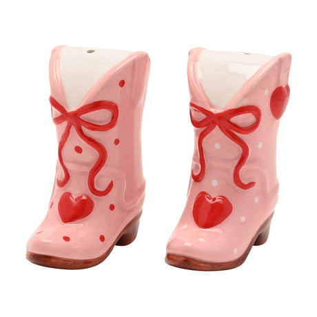 Pink ceramic cowboy boot salt and pepper shaker set with red bow, red heart on the toe, and polka dot detailing, shown on a white background.