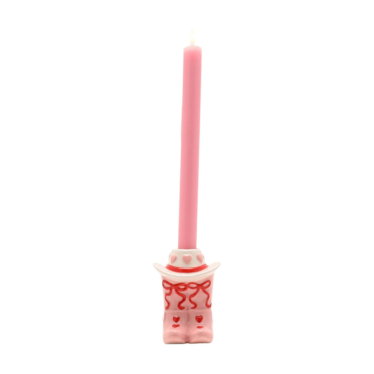 Ceramic taper candle holder shaped as pale pink cowboy boots with red heart and bow details beneath a white cowboy hat, holding a lit pink taper candle, on a plain white background.