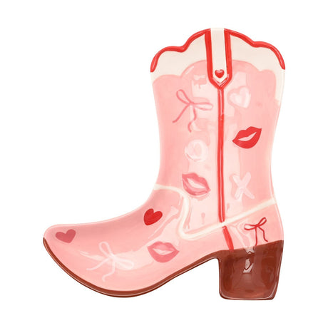 Cowgirl boot earthenware plate in pink with white top band, red seam, brown heel, and scattered hearts, lip prints, bows, and pale O and X motifs on a white background.