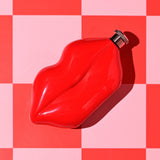 Red steel hip flask shaped like pouting lips with a knurled silver screw cap, glossy finish, 5oz capacity, shown on a red and pink checkered background.