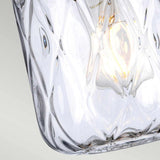 The Sola 1 Light Pendant, with its clear glass encasement adorned in elongated ovals, showcases a delicate dance of light reflections. Its polished nickel accents add a touch of elegance as it hangs against a soft gradient backdrop.
