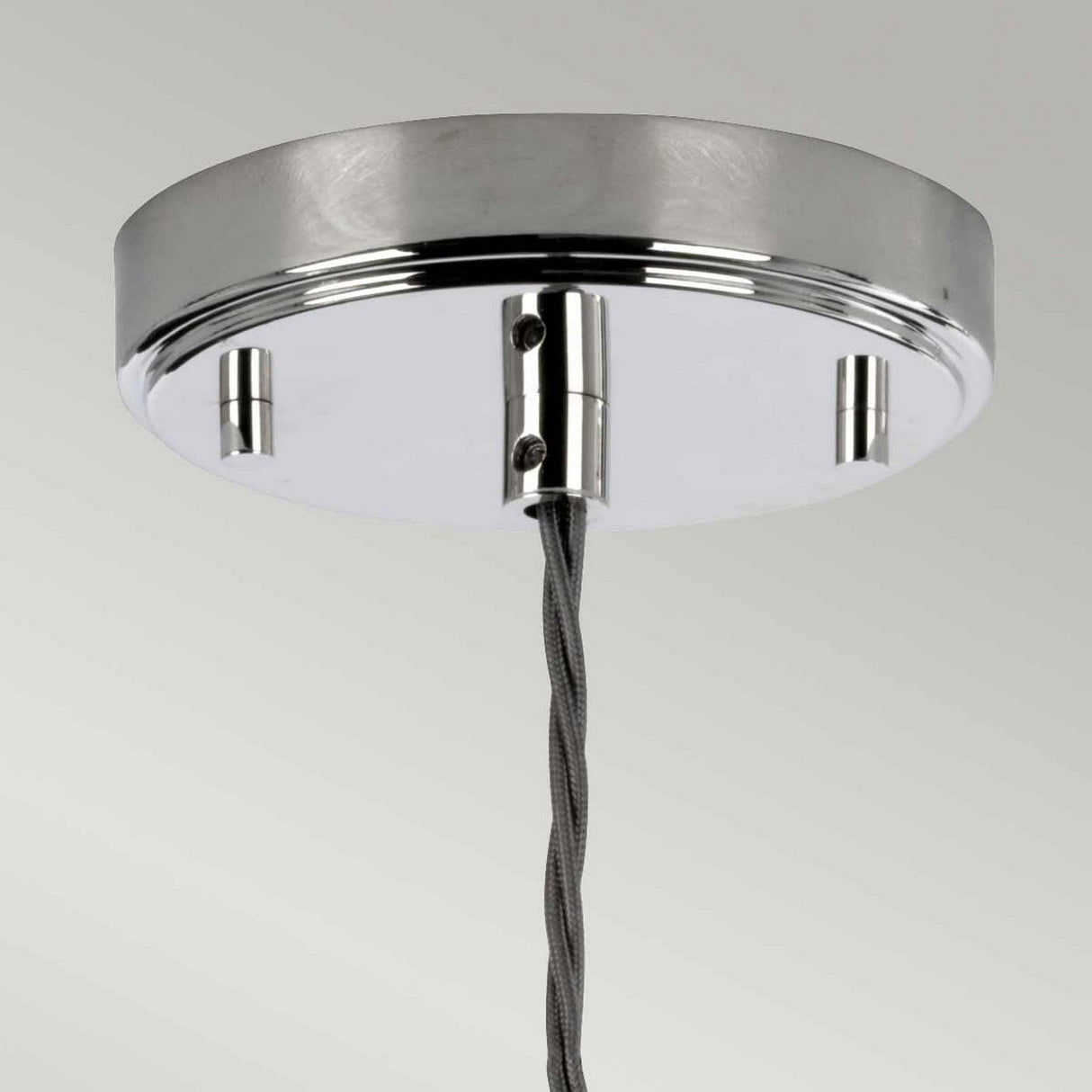 A modern Sola 1 Light Pendant in polished nickel with clear glass accents and a braided gray cable elegantly suspends against a light gray backdrop, showcasing its minimalist design.