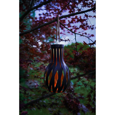 Solar LED Table Lamp 27cm in Black & Gold, lantern-shaped with twisted black steel strips and glowing gold interior, hanging by rope from a tree branch outdoors.