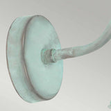 A close-up view of the Somerton 1 Light Outdoor Wall Light highlights its greenish verdigris metal mount, featuring a round base and curved arm that suggests it might be crafted from bronze or copper, adding an air of elegance and age.
