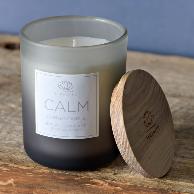 Calm Bergamot, Lavender & Sandalwood Scented Candle 120g in a round frosted blue-grey jar with printed label, shown beside its wooden lid on a wooden surface.