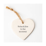 White ceramic heart-shaped hanging plaque with grey "Relax & live in the moment" text and a rustic twine loop, shown against a plain white background.