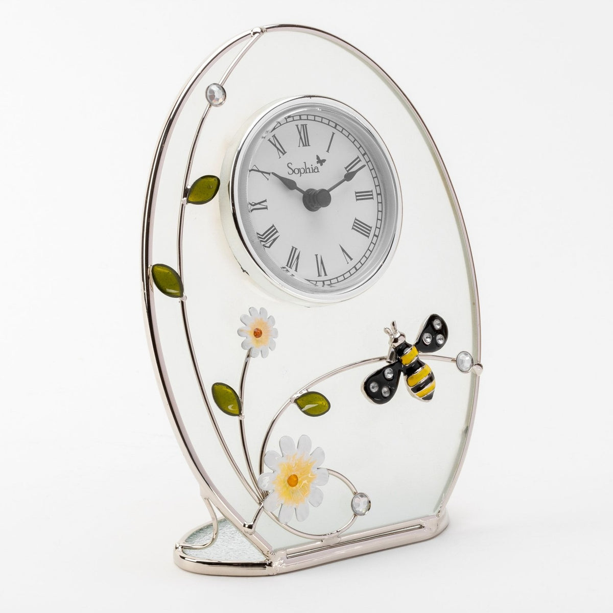 Oval mantel clock with frosted white glass panel and silver-coloured wire frame, featuring a Roman numeral dial, enamel daisies, leaves, and a bumble bee, on a plain white background.