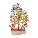 Large multi-coloured gemstone tree ornament with gold-coloured wire branches holding chip stones in bands from purple and blue to green, yellow and red-brown, set on a white stone base.