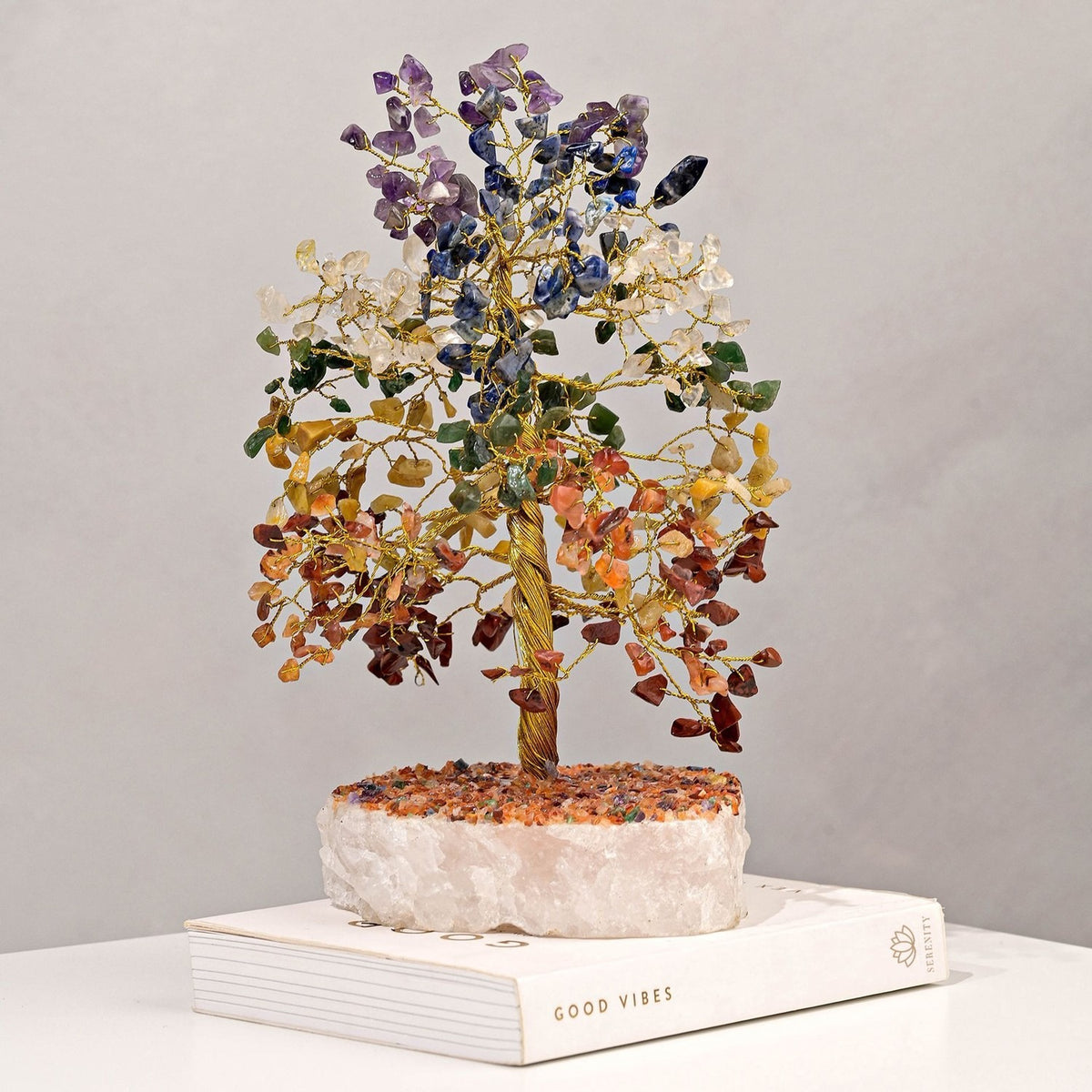 Large multi-coloured gemstone tree ornament with a twisted gold-coloured wire trunk, branches set with purple, blue, clear, green, yellow, orange and red-brown chips, on a white crystal base.