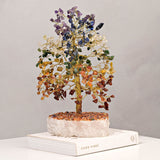 Large multi-coloured gemstone tree ornament with a twisted gold-coloured wire trunk, branches set with purple, blue, clear, green, yellow, orange and red-brown chips, on a white crystal base.
