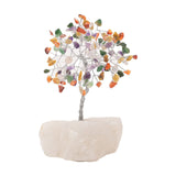 Small multi-coloured gemstone tree ornament with a rounded canopy of purple, orange, green and yellow chips on a twisted silver-toned trunk, set in a white stone base against a plain white background.