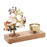 7 Chakras Gemstone Tree wooden tea light candle holder with gold-wire branches holding coloured stone chips, lit candle in a brass cup on a rectangular base, white background.