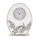 Oval mantel clock with clear glass panel and silver frame, white Roman numeral dial, and silver leaf and daisy details with pearl-effect centres, on a white background.