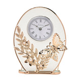 Oval mantel clock with white Roman numeral dial, frosted clear glass body, and gold-toned leaf, flower and butterfly decoration with pearl centres, on a plain background.