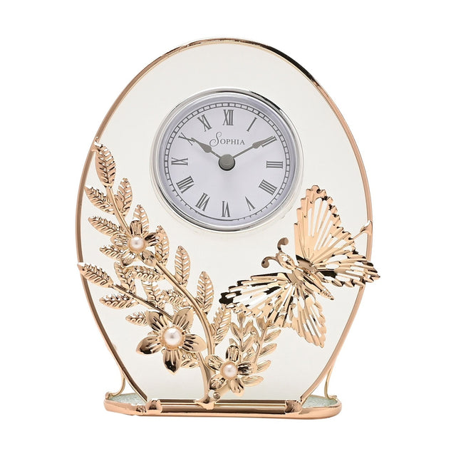 Oval mantel clock with white Roman numeral dial, frosted clear glass body, and gold-toned leaf, flower and butterfly decoration with pearl centres, on a plain background.