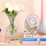Classic Gold Butterfly and Flower Oval Mantel Clock with clear glass face, white dial and Roman numerals, displayed atop stacked books beside a glass vase of white roses.