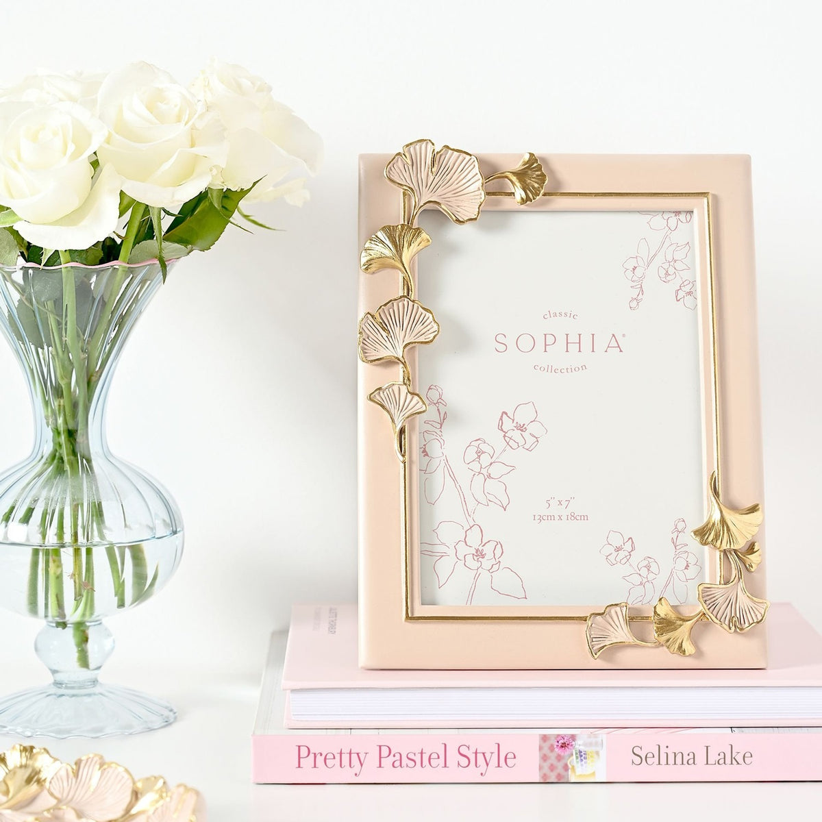 Classic Ginkgo Resin Photo Frame in pink with gold and pink gingko leaf details at the corners, shown beside white roses and a stacked pink book on a light surface.