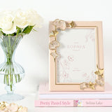 Classic Ginkgo Resin Photo Frame in pink with gold and pink gingko leaf details at the corners, shown beside white roses and a stacked pink book on a light surface.