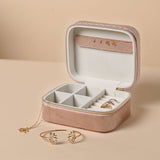 Open pink velvet rectangular jewellery box with gold-tone zip, cream lining, ring slots and compartments, shown with a lotus bangle and pendant necklace.