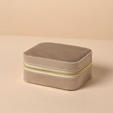 Rectangular brown velvet jewellery box with rounded corners and a gold-coloured zip with pull tab around the front and sides, shown closed on a plain beige background.