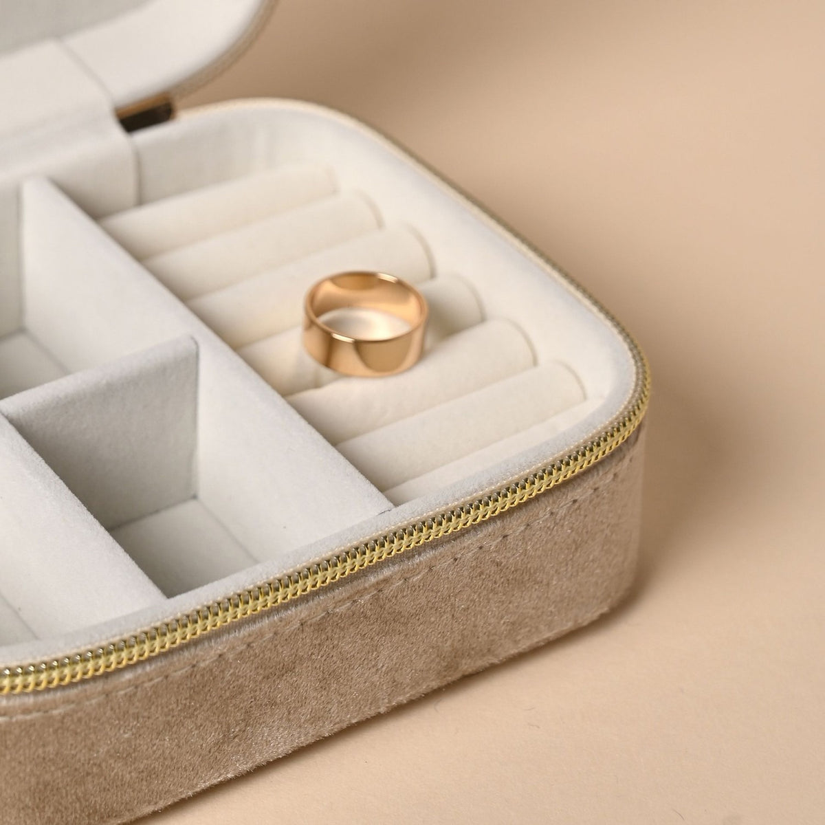 Rectangular zip velvet jewellery box in brown with gold-tone zip, open to show cream interior with ring rolls and compartments holding a gold ring.