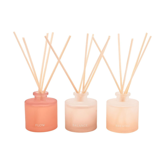 Set of three round frosted reed diffusers in peach tones labelled Flow, Balance and Breathe, each with natural reeds fanned out, shown on a plain white background.