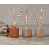 Set of three frosted peach reed diffusers labelled Flow, Balance and Breathe, each with natural reed sticks, shown on a neutral surface with a draped linen cloth.