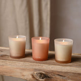 Set of three round frosted glass votive candles labelled Balance, Flow and Breathe, in off white, cream and terracotta tones, lit on a wooden shelf.