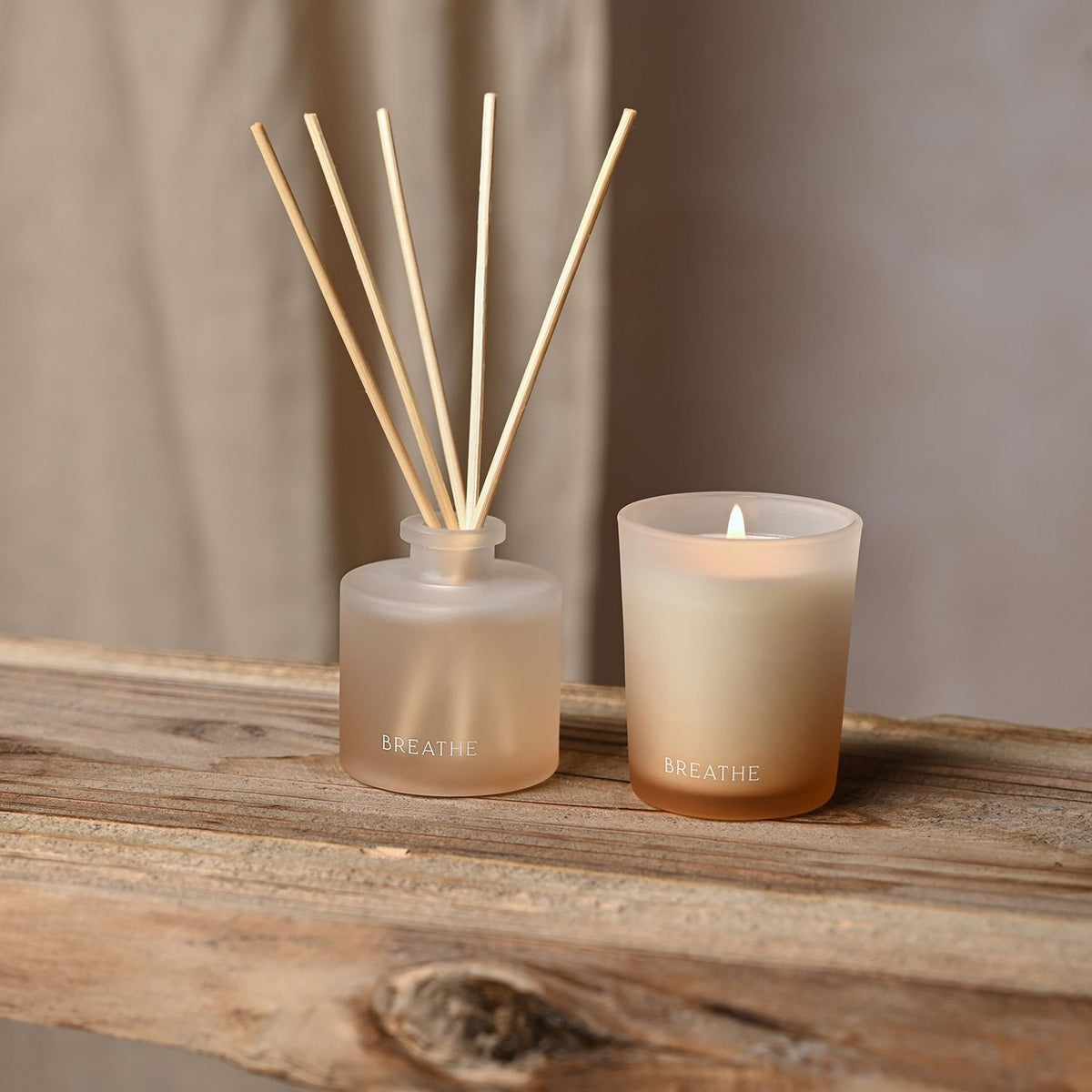 Breathe Frosted Candle and Reed Diffuser Set in off white glass, lit candle beside a diffuser bottle with wooden reeds, both labelled "BREATHE", on a wooden shelf.